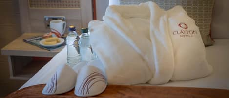 A hotel room with a bed, a bedside table with a magazine, two bottles of water, and a towel with the hotel name.