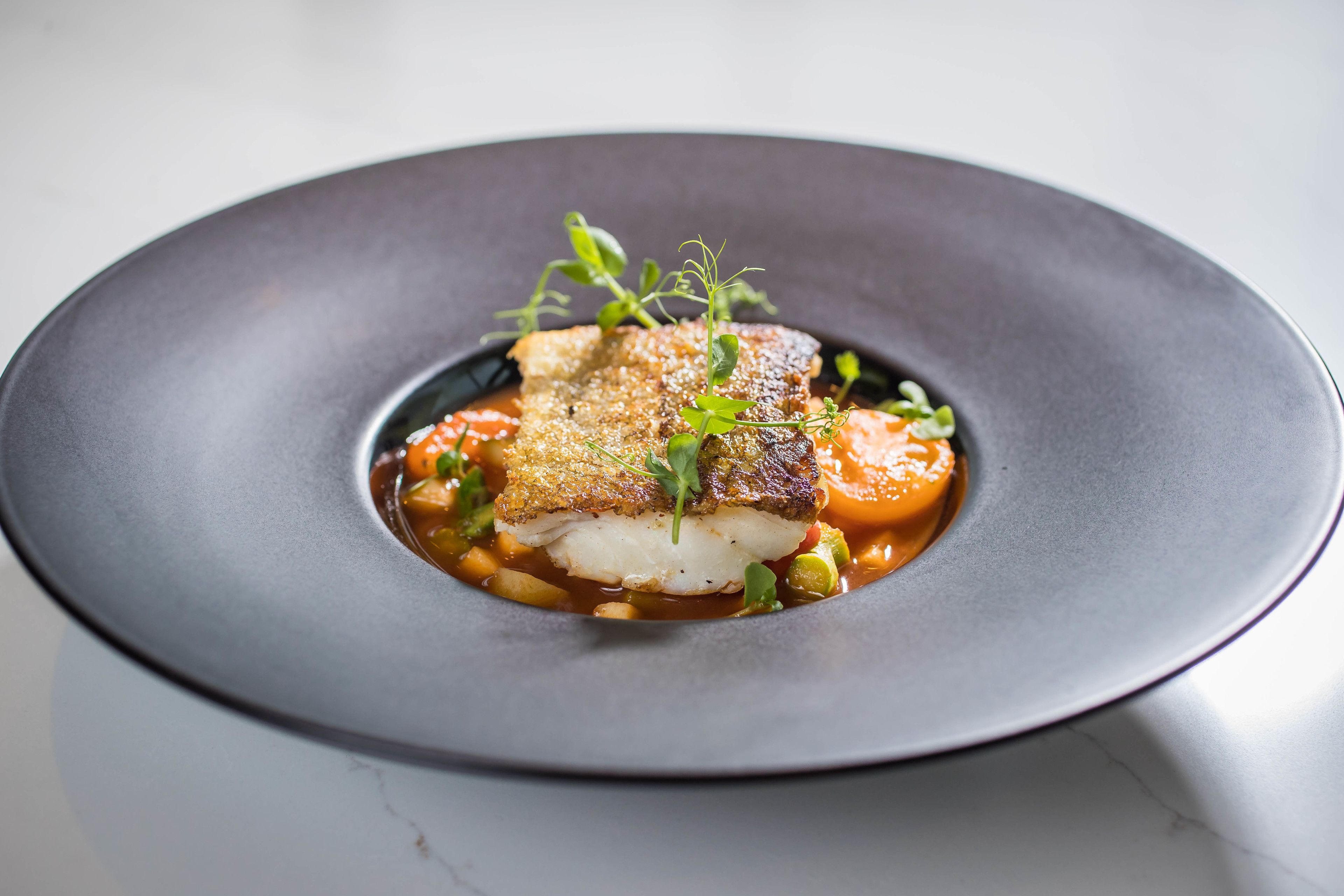 Un plato de comida con un trozo de pescado, verduras y una guarnición.
