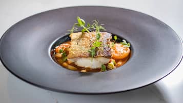 Un plato de comida con un trozo de pescado, verduras y una guarnición.