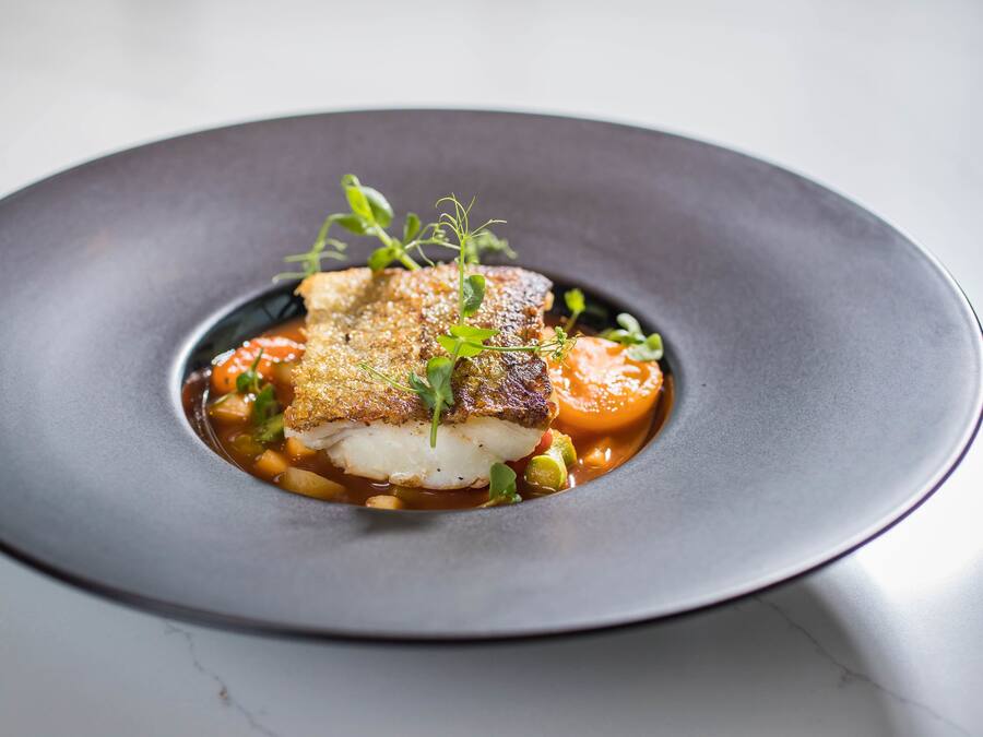 A plate of food with a piece of fish, vegetables, and a garnish.