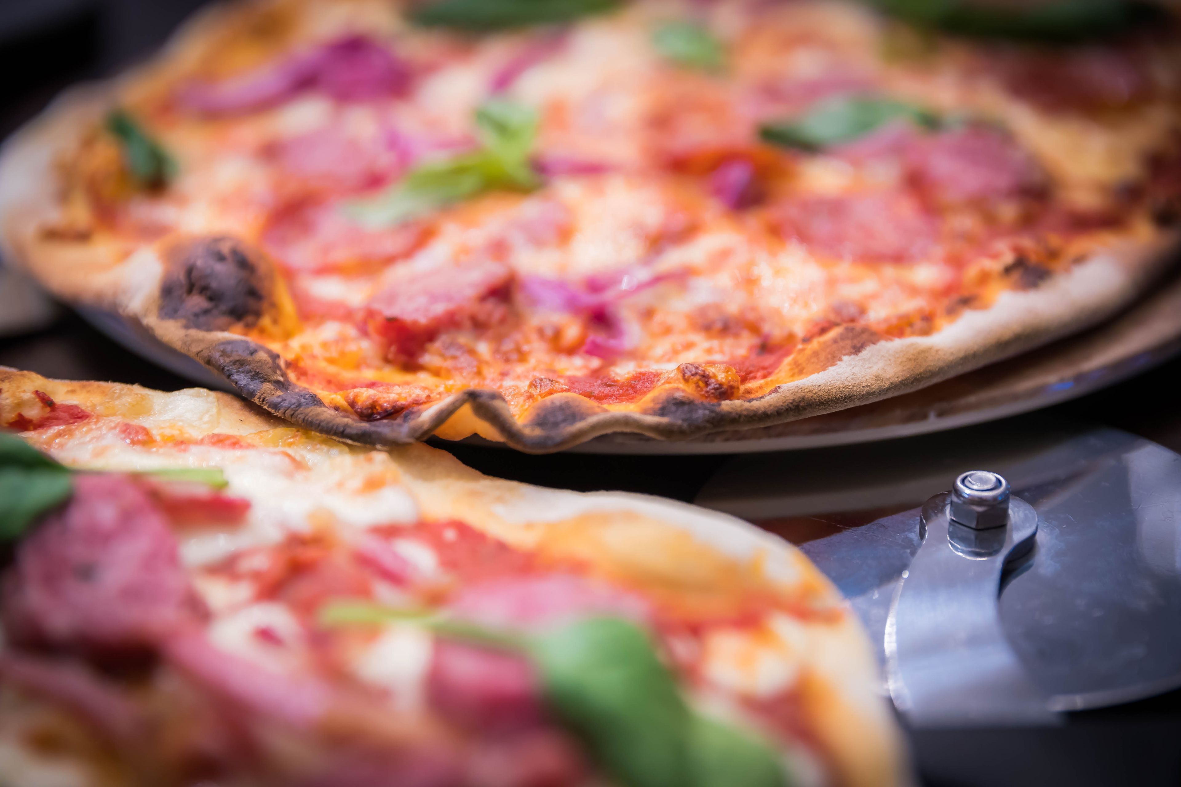 Una pizza con ingredientes visibles y un cortador de pizza sobre una bandeja.