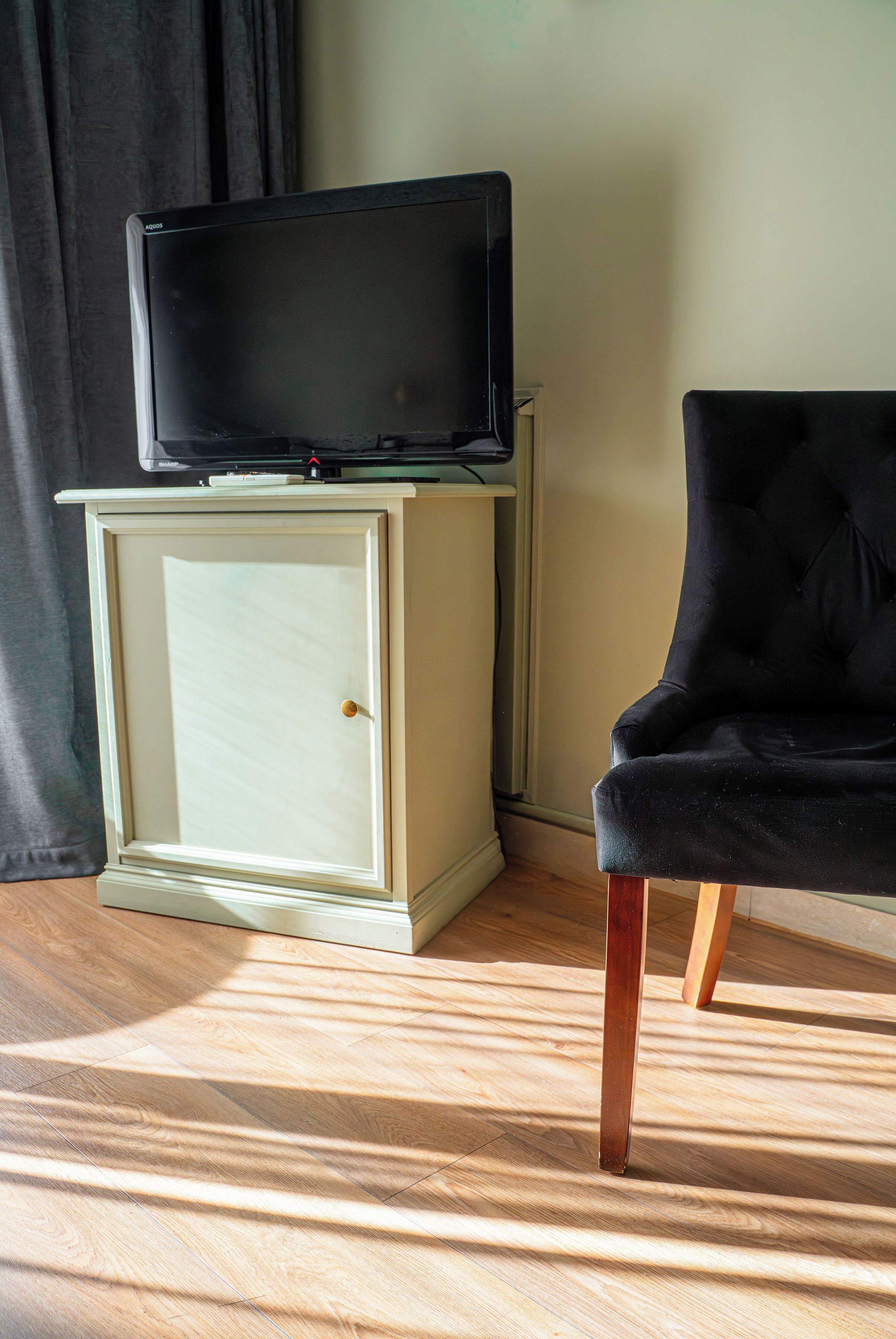 A television on a cabinet, a black chair, and a wooden floor.