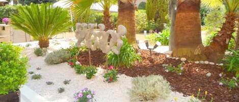 A landscaped garden with palm trees, a decorative stone sculpture, and various shrubs and flowers.