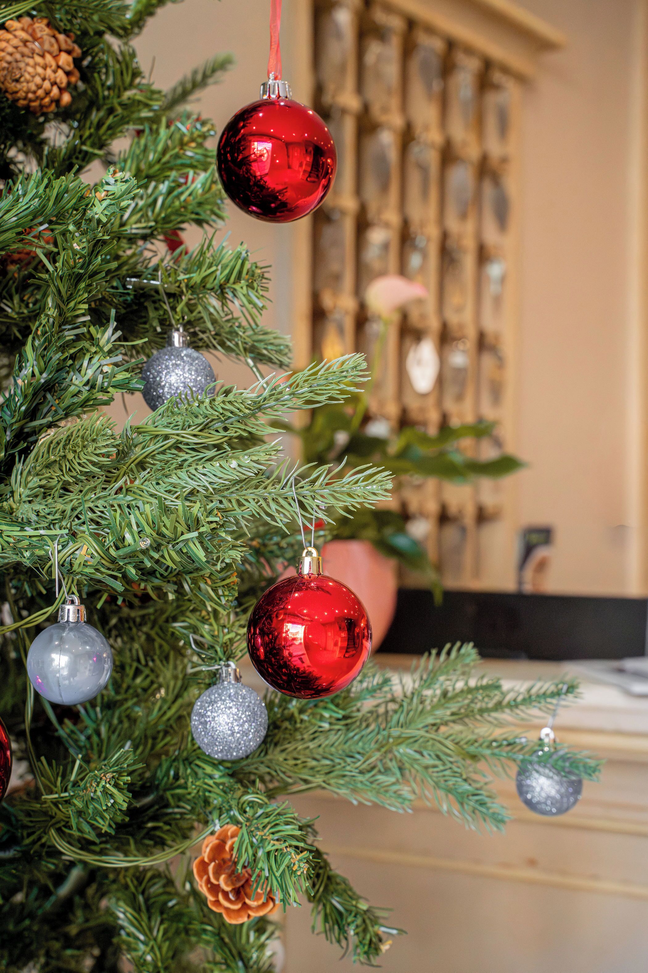 A Christmas tree with red and silver ornaments, a pine cone, and a blurred background with a fireplace.