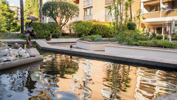 A serene courtyard with a reflective water feature, surrounded by lush greenery and modern buildings. - Hotel Diana (Vence)