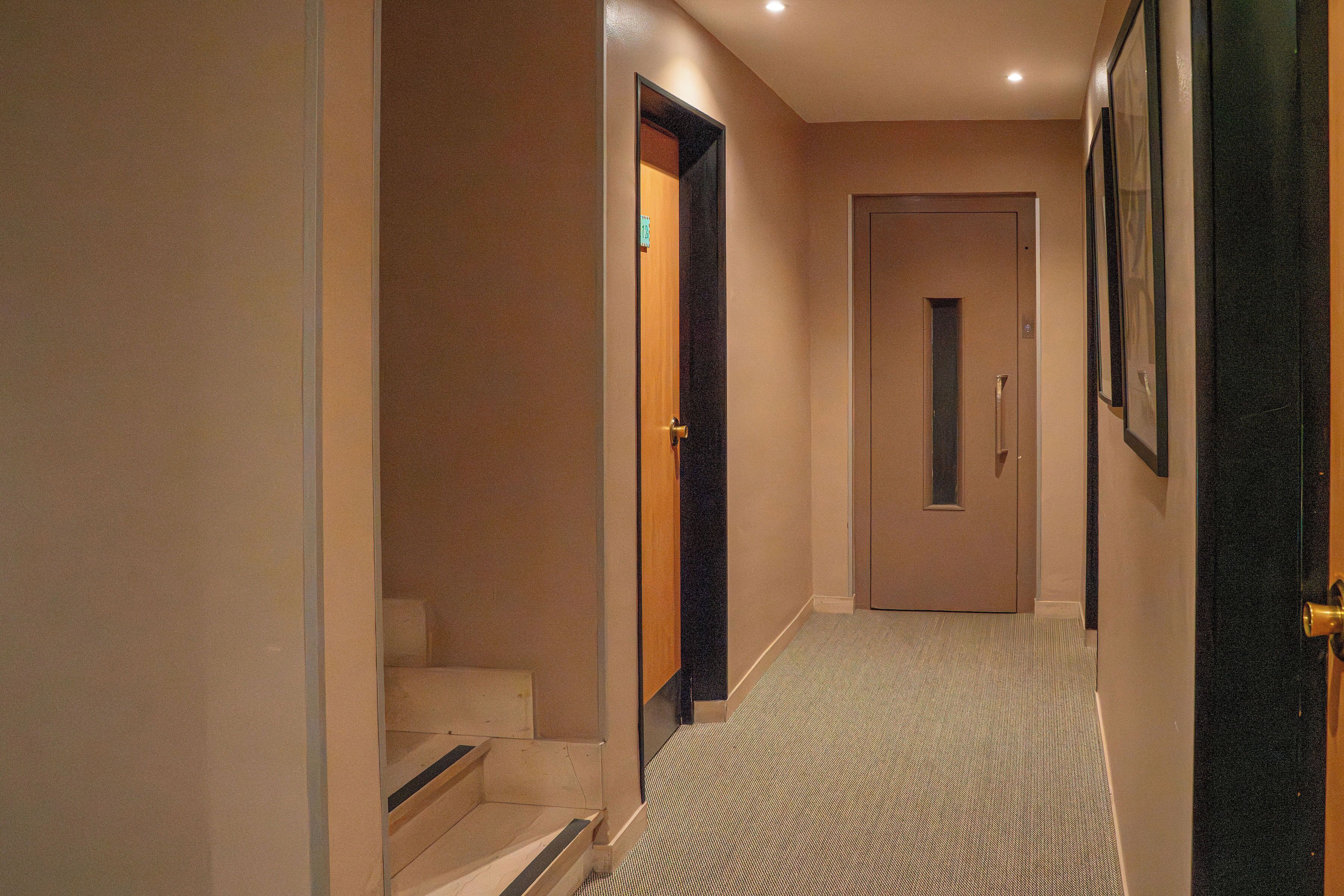Un pasillo con piso alfombrado, una puerta de madera y una escalera que conduce a un nivel superior.