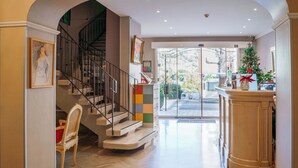 A hotel lobby with a staircase, a reception desk, and a Christmas tree. - Hotel Diana (Vence)