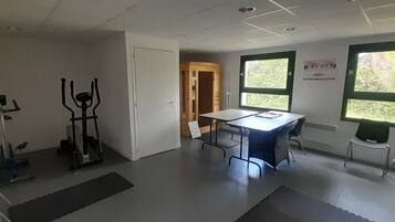 A room with a white door, a table with chairs, exercise equipment, and a window with a view of greenery.
