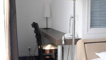 Une chambre d’hôtel avec un lit, un bureau, une chaise, une lampe et un tapis à rayures.