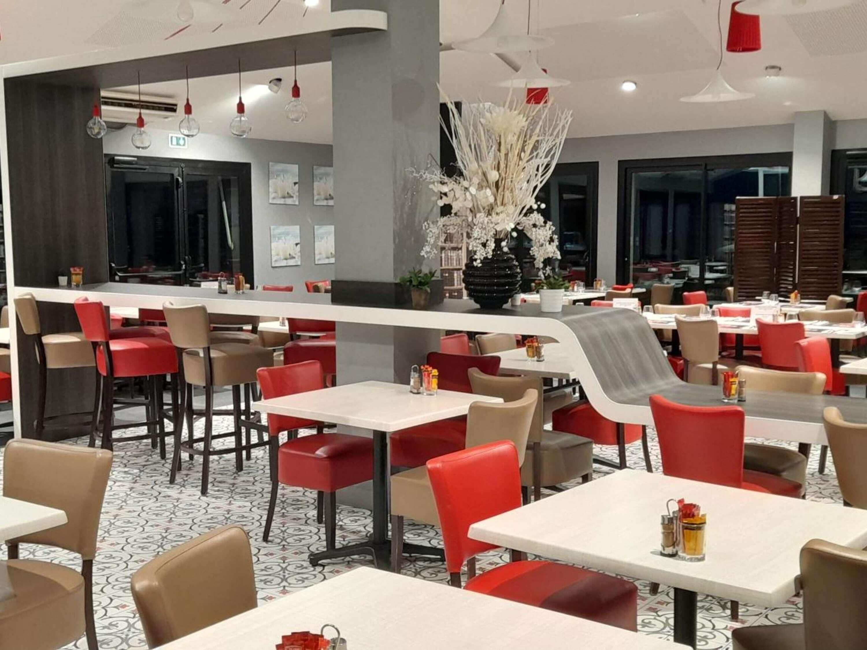 Un área de comedor moderna con varias mesas y sillas, una planta decorativa en el centro y un suelo estampado.