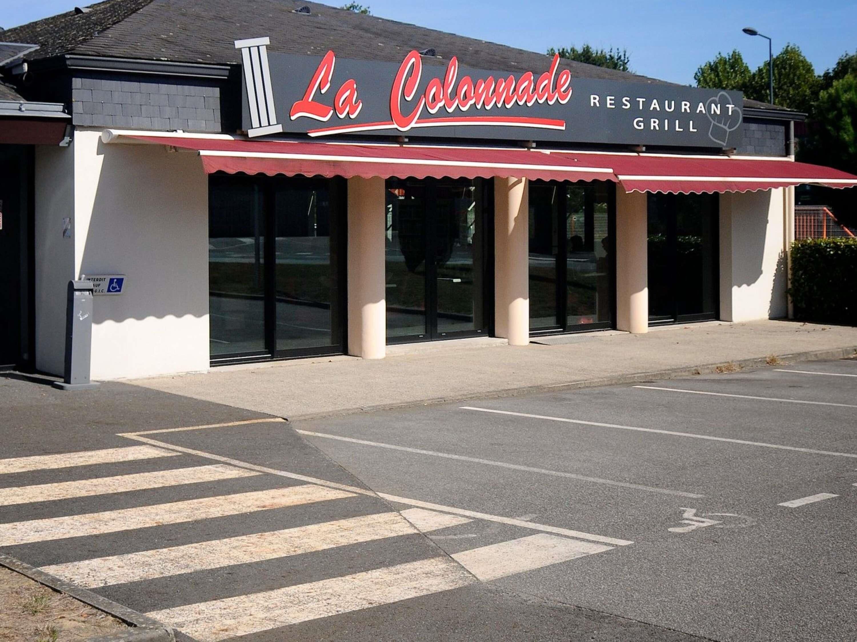 En restaurang som heter ”La Colonnade”, med ett rött markis, en skylt som visar att den är tillgänglig för personer med funktionsnedsättning och ett tydligt övergångsställe för fotgängare.