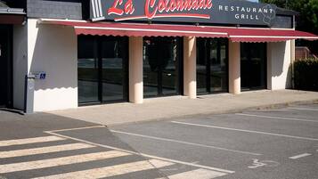 En restaurang som heter ”La Colonnade”, med ett rött markis, en skylt som visar att den är tillgänglig för personer med funktionsnedsättning och ett tydligt övergångsställe för fotgängare.