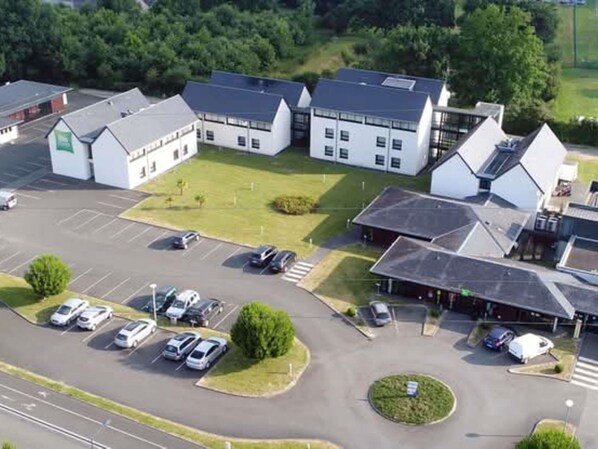 An aerial view of a building complex with multiple white structures, a parking lot with several cars, and surrounding greenery. - ibis Styles Segre (Segré-en-Anjou-Bleu)