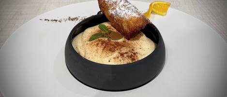 Un postre en un tazón negro sobre un plato blanco, decorado con un toque de azúcar glas y una rodaja de limón.