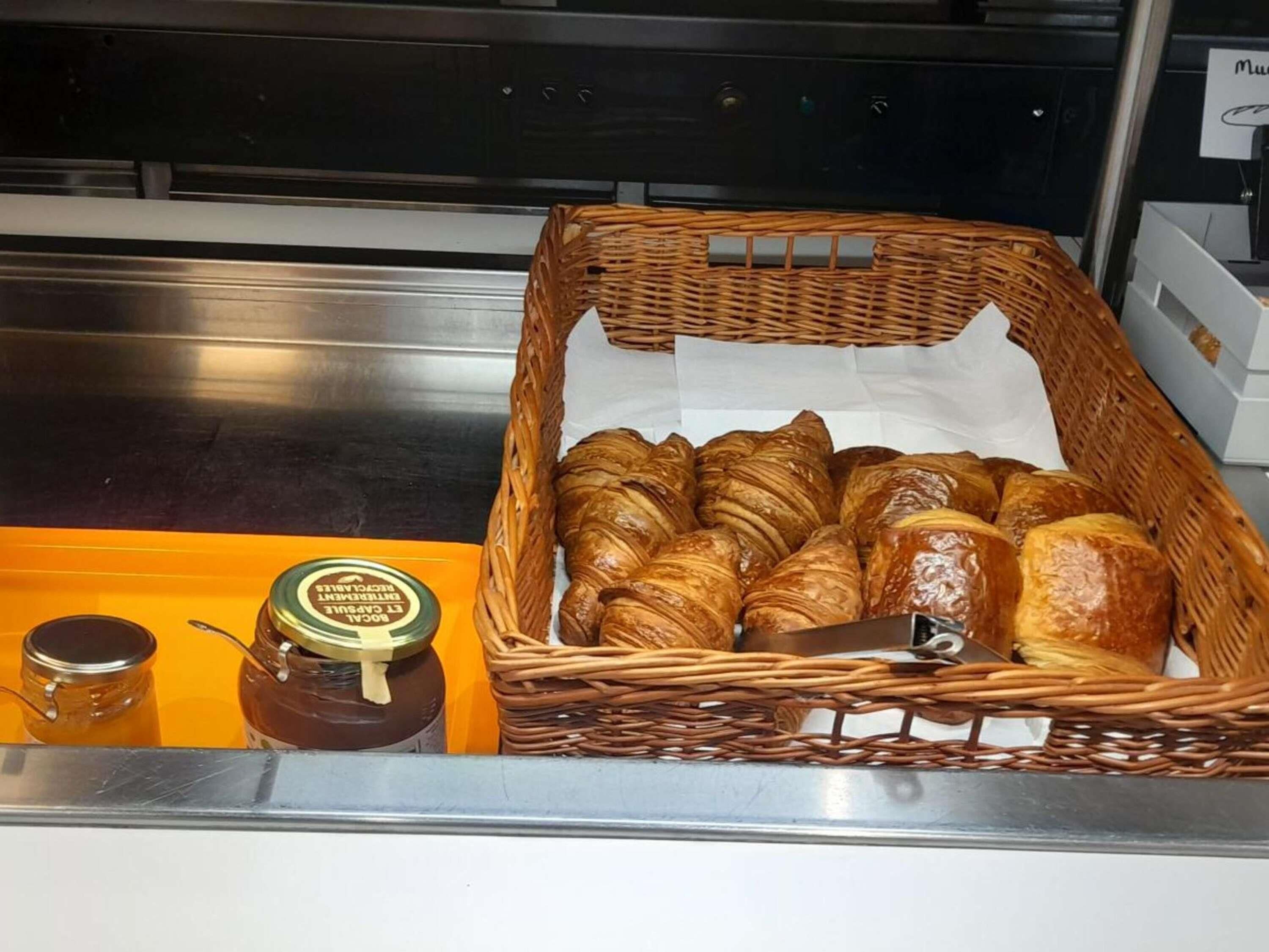 A basket of croissants and two jars of honey on a tray.