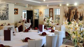 Un restaurante con mesas redondas, manteles blancos y servilletas rojas.