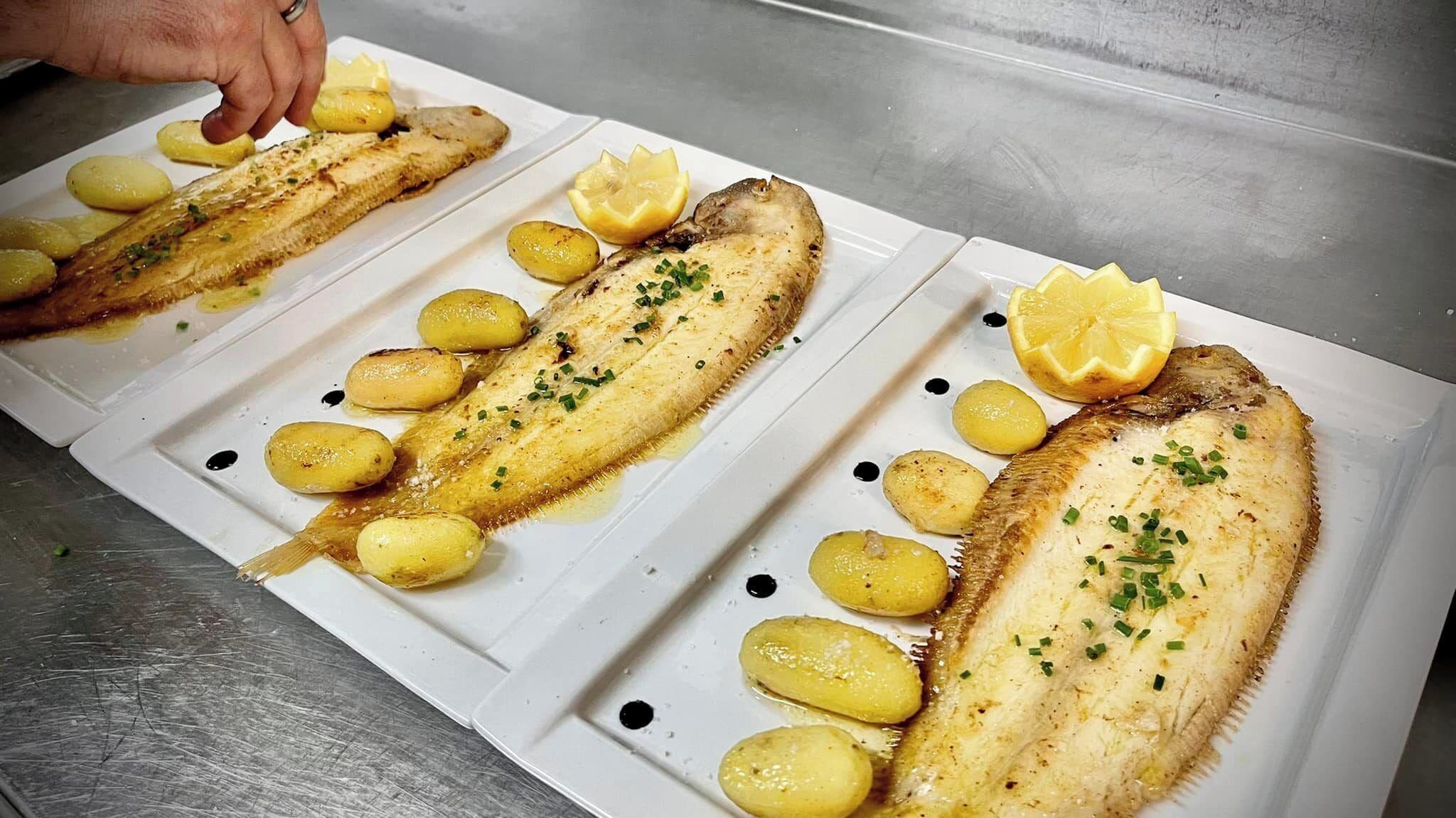 Un plato blanco con filetes de pescado a la parrilla, rodajas de limón y patatas asadas.