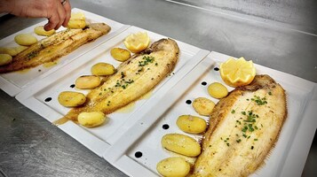 Un plato blanco con filetes de pescado a la parrilla, rodajas de limón y patatas asadas.