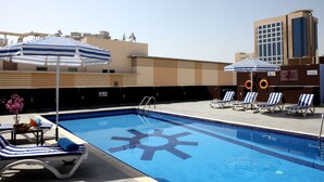 A rooftop pool with blue and white striped lounge chairs, umbrellas, and a sign indicating a no diving area. - Royal Ascot Hotel Apartment (Dubai)