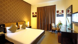 A hotel room with a large bed, a desk with a chair, a TV, and a window with curtains. - Royal Ascot Hotel Apartment (Dubai)