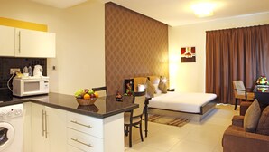 A compact hotel room with a kitchenette, a bed, a dining area, and a living space. - Royal Ascot Hotel Apartment (Dubai)