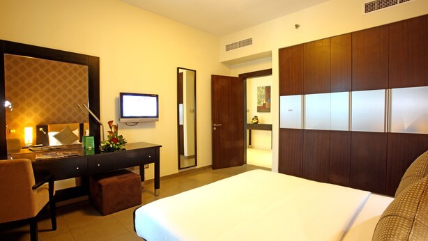 A hotel room with a large bed, a desk with a computer, a chair, a mirror, and a wardrobe. - Royal Ascot Hotel Apartment (Dubai)