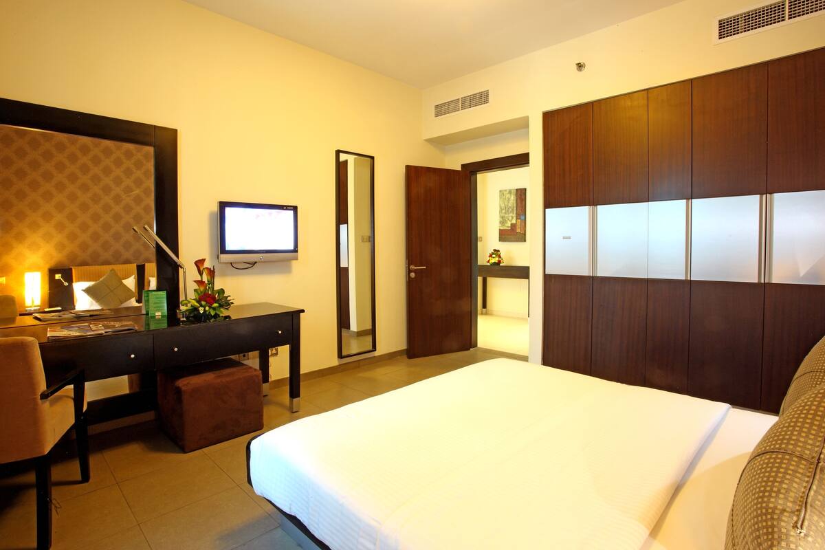 Une chambre d’hôtel avec un grand lit, un bureau avec un ordinateur, une chaise, un miroir et une armoire.
