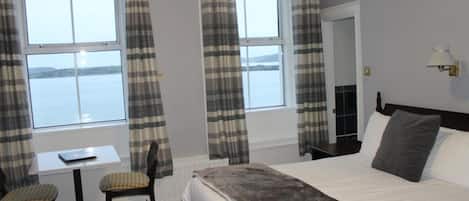 A hotel room with a bed, a table, two chairs, and a view of the sea through large windows.