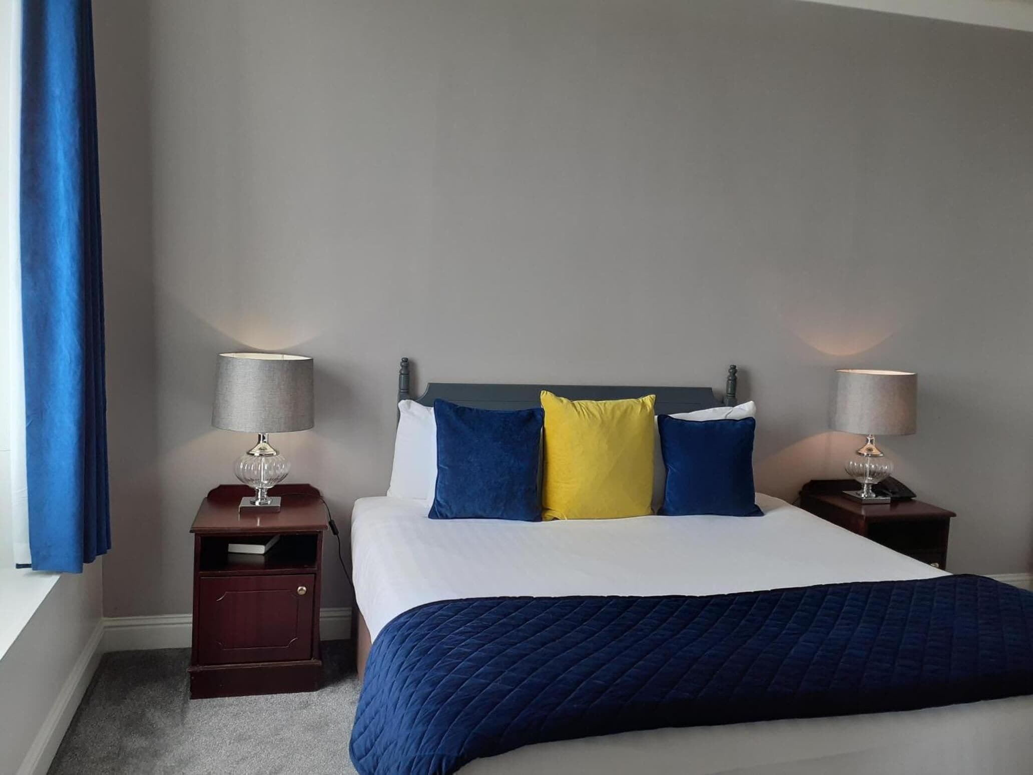 A neatly made bed with a blue quilt, two bedside lamps, and a nightstand with a lamp.