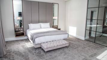 Un dormitorio moderno con una cama grande, una mesita de noche, un espejo y un separador de vidrio.