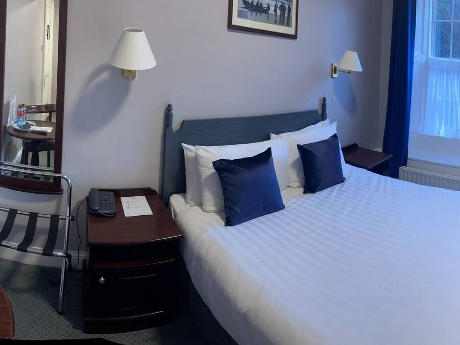 A hotel room with a bed, bedside tables, a chair, a window with curtains, and a door.