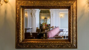A mirror with an ornate gold frame reflecting a dining area with striped seating and a long table. - Commodore Hotel (Cobh)