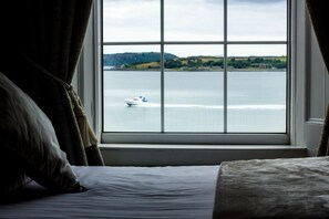 Une chambre avec une grande fenêtre donnant sur une étendue d’eau et sur des collines lointaines.