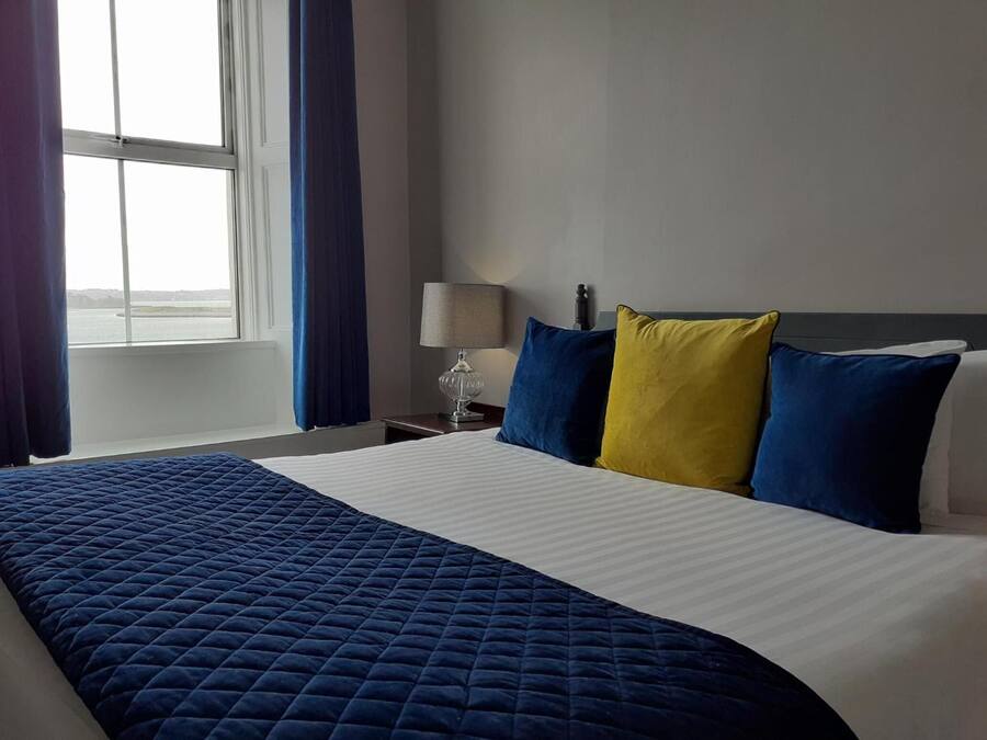 Habitación de hotel con cama, mesita de noche, lámpara y vista al mar a través de una ventana.