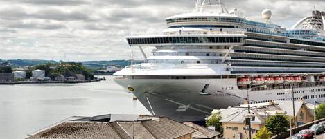 A large cruise ship docked at a port with a cityscape in the background.