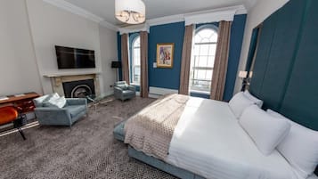 A hotel room with a large bed, a desk, a chair, a fireplace, and large windows with curtains.