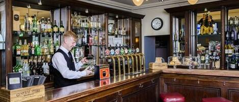 A bar with a bartender, a beer tap, and a shelf with various bottles.