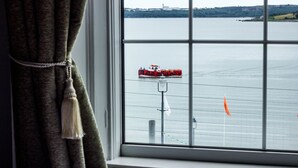 A view of a red boat on a body of water through a window with a curtain. - Commodore Hotel (Cobh)