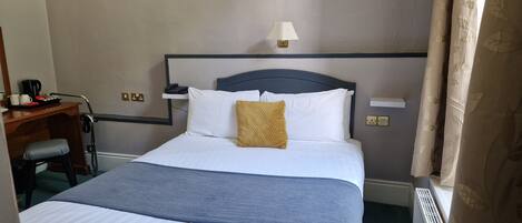 A neatly made bed with white and blue bedding, a bedside lamp, and a small table with a coffee maker and cups.