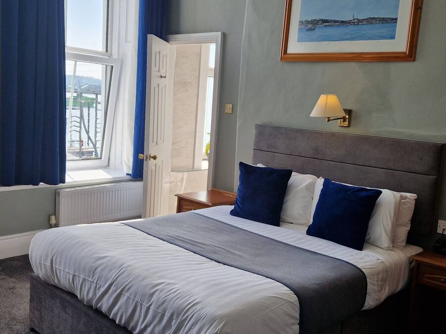 A hotel room with a bed, a nightstand, a lamp, a window with curtains, and a framed picture on the wall.