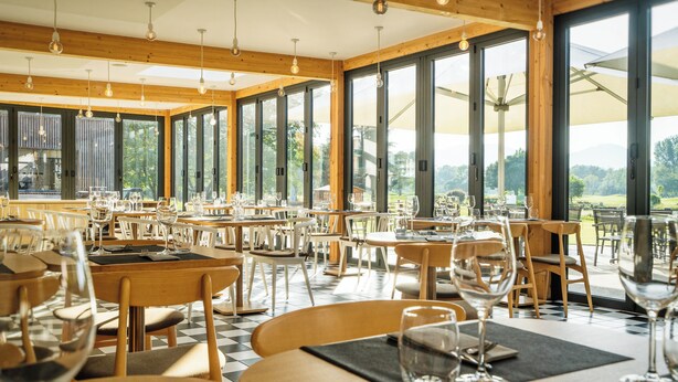 A restaurant with large windows, wooden tables, and chairs.