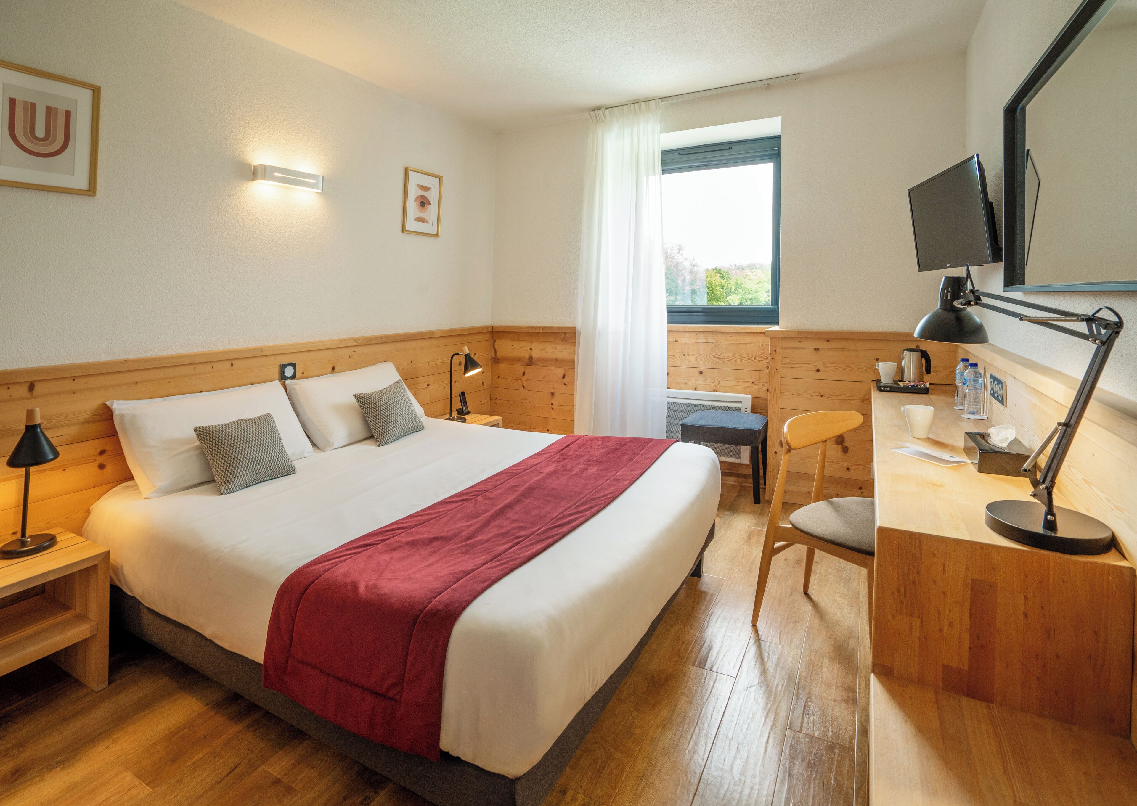 A hotel room with a large bed, a desk, a chair, a TV, and a window with curtains.