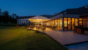 A modern building with large glass windows, outdoor seating area with umbrellas, and a well-maintained lawn.