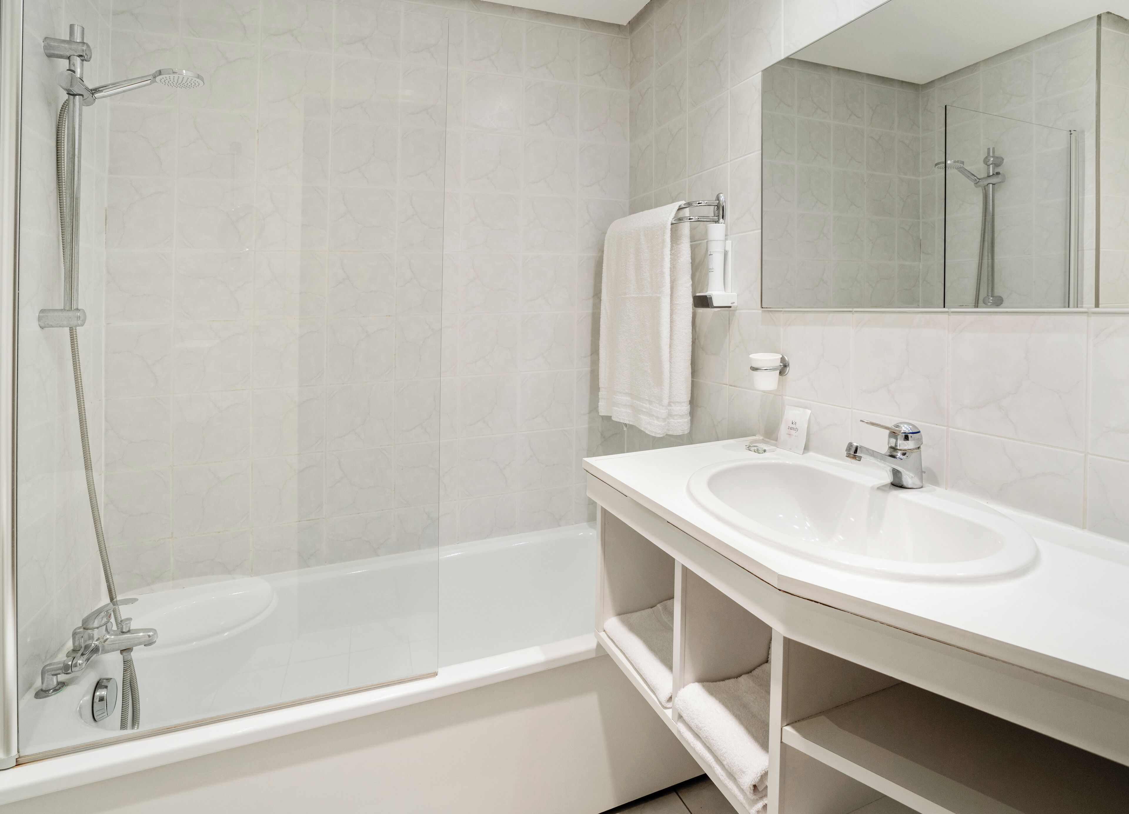 Un baño moderno con ducha de mampara de vidrio, lavabo blanco y espejo.