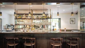 A bar area with three wooden chairs, a variety of bottles and glasses on shelves, and hanging pendant lights.