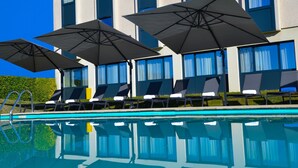 A poolside area with lounge chairs and umbrellas, a clear blue sky, and a building with large windows.