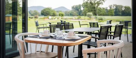 An outdoor dining area with tables and chairs, a view of a golf course, and a mountain in the distance.