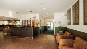 A modern hotel lobby with a reception desk, seating area, and a bar.