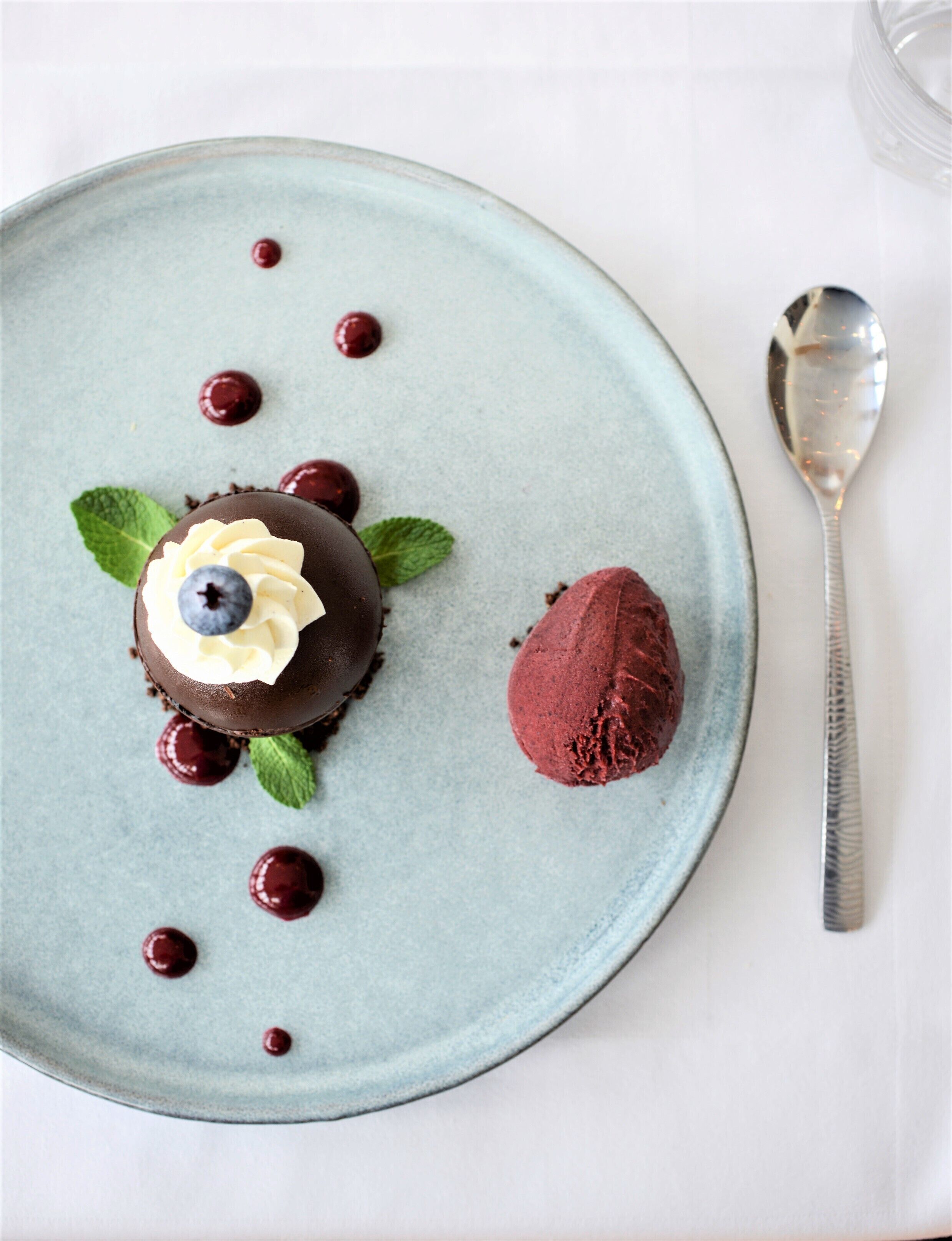 Un plato de postre con una esfera de chocolate, una bola de helado rojo y cerezas.