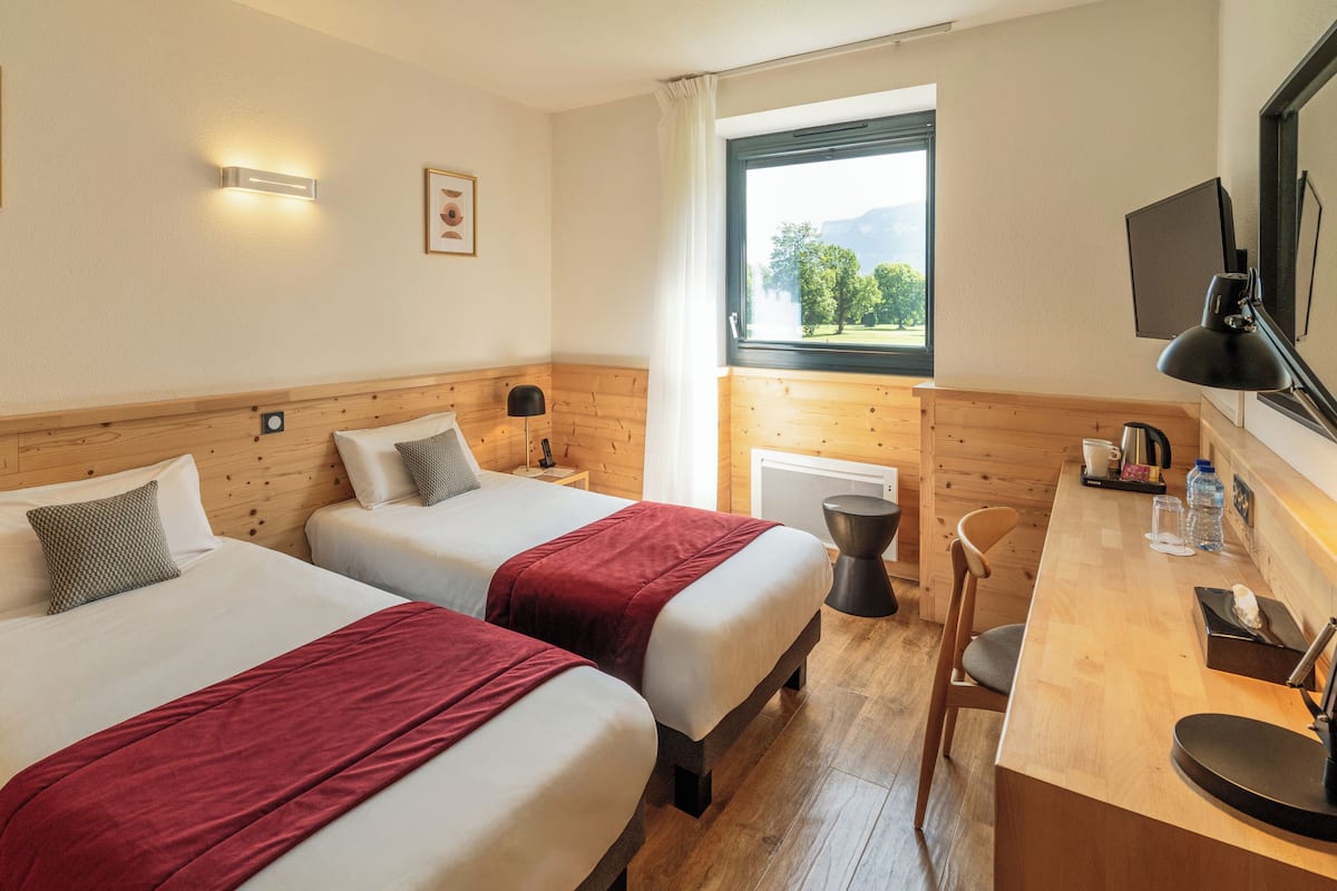 Habitación de hotel con dos camas, un escritorio, una silla, un televisor y una ventana con vistas a árboles.